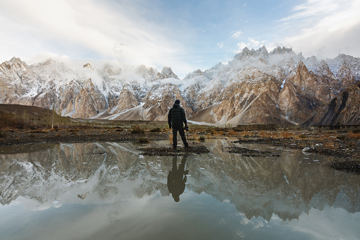 Young photographer looking at Passu Cathedral mountain in Pakistan and reflection on the water