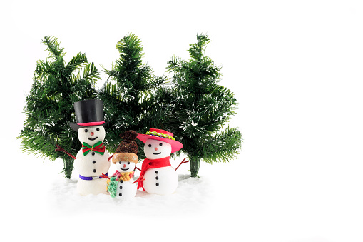 Winter scene of a three Snowmen family figures with fir trees and artificial snow isolated on white background