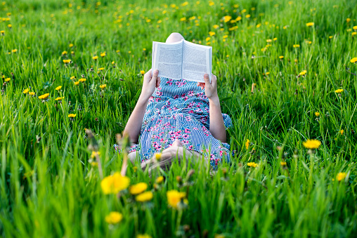 Young blond girl lying down in grass field outdoors reading a book