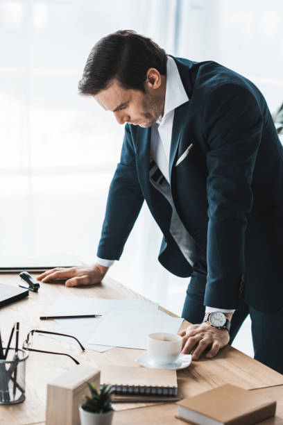 istock Businessman in suit leaning on table with business papers 949854198