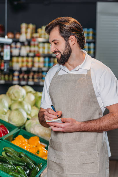 istock smiling shop assistant in apron with notebook in supermarket 949875480