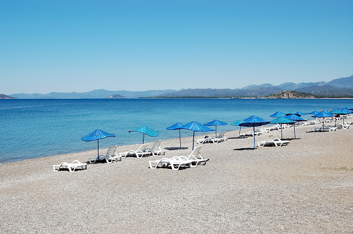 Beach with blue umbrellas on the Mediterranean coast in Fethiye, Turkey.