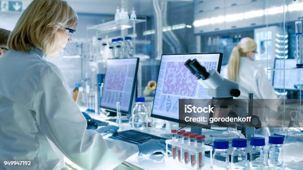 Senior Female Scientist Works With High Tech Equipment In A Modern Laboratory Her Colleagues Are Working Beside Her Stock Photo - Download Image Now