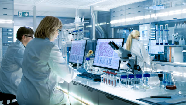 istock Female and Male Scientists Working on their Computers In Big Modern Laboratory. Various Shelves with Beakers, Chemicals and Different Technical Equipment is Visible. 949947214