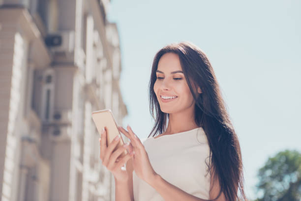 istock Smiling woman reading message on  mobile phone while standing on  the street 949951538