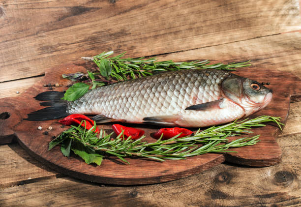 Fresh fish with herbs and pepper before cooking on wooden background stock photo