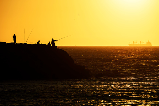 Fishing in the sunset on the ocean. A group of anglers on a rock in the Indian Ocean. Unrecognizable people. Cottesloe, Perth, Western Australia