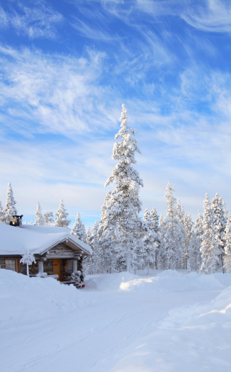 A hut in a snowy field with rocky mountains and a thick forest