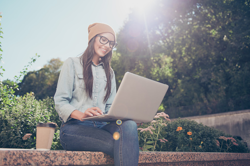 Happy hipster young woman working on laptop in the park