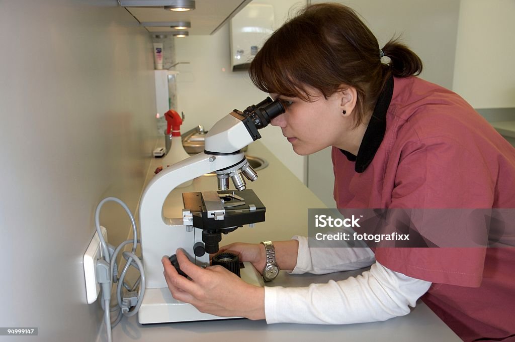 Joven enfermera espera a través de un microscopio - Foto de stock de Microscopio libre de derechos