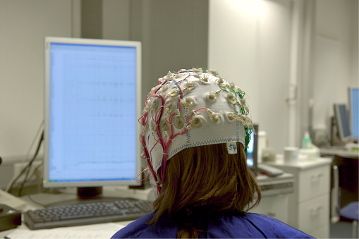 for a scientific experiment, a girl is connected with cables to a computer, EEG for research, looks to the own waves on a screen