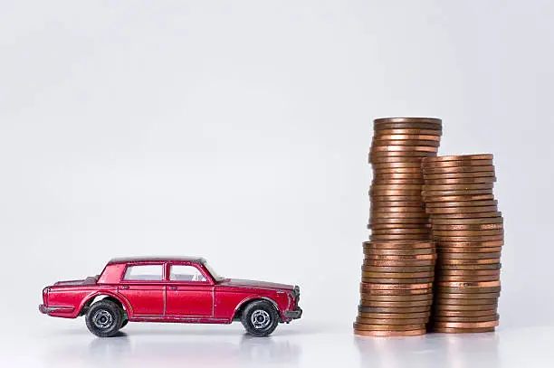 Beaten up red miniature rolls royce silver shadow (toy car) standing next to a pile of coins. Depicting wealth and poverty. White background.