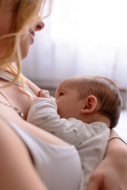 bambino che allatta al seno da vicino. bella madre che tiene in braccio il suo neonato. mamma che allatta il bambino. bella donna e neonato si rilassano a casa. madre bionda che allatta il bambino. - mother new baby nursery foto e immagini stock