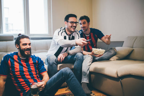 istock Friends in soccer jerseys holding remote control and smiling 950020568