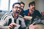 Man shouting and watching soccer game with friends with betting slip in his hand