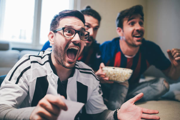 Man shouting and watching soccer game with friends with betting slip in his hand Excited friends watching football game and holding betting slip and popcorn sports betting stock pictures, royalty-free photos & images
