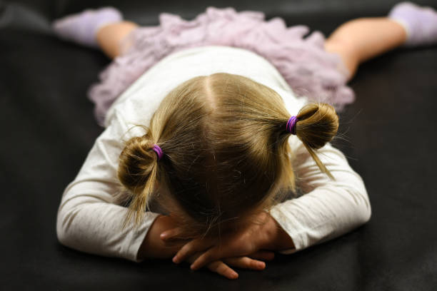 床に横に�なっていると、黒の背景で泣いている子供の女の子が動揺してください。 - tantrum ストックフォトと画像