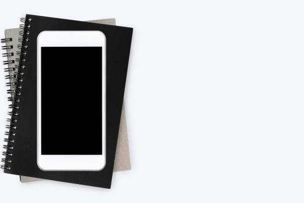 istock Smartphone with blank screen is on top of notebooks on white table. Top view with copy space, flat lay. 950050090