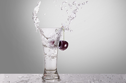 Splash of water in a glass with a cherry on a gray background