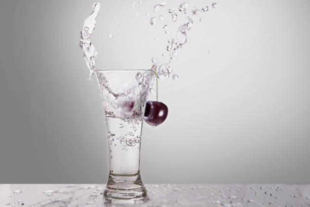 Splash of water in a glass with a cherry on a gray background stock photo