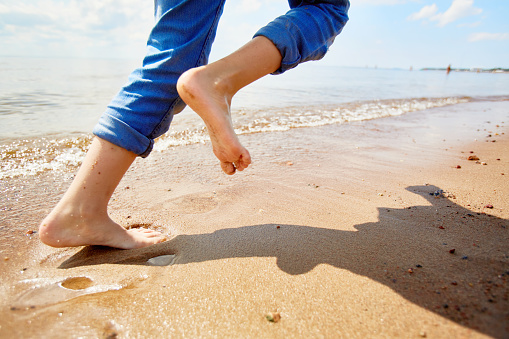 Barefoot child running on sandy beach along coastline while enjoying summer vacation or weekend