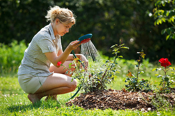 Beautiful woman fills a bucket with water to water her garden, looking at camera
