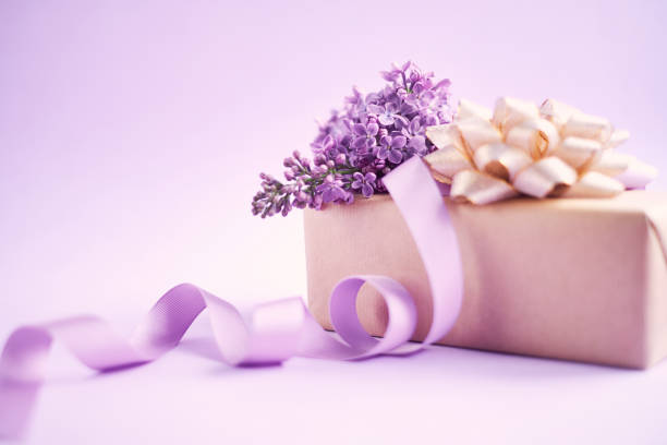 Arreglo para el día de la madre con flores lilas y un regalo envuelto - foto de stock