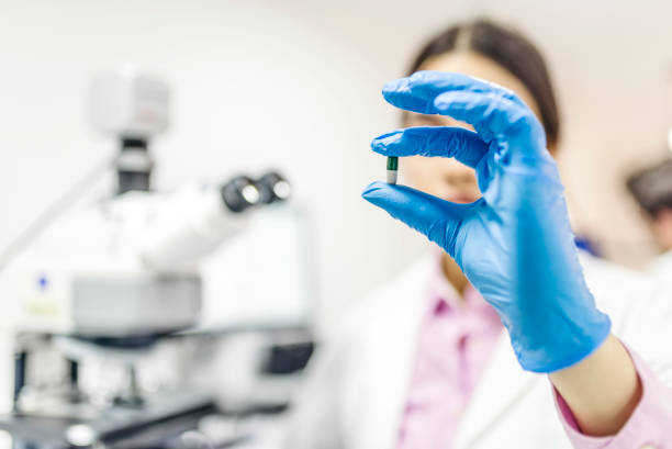 Young attractive female scientist holding a pill Science, chemistry, biology, medicine and people concept - close up of young female scientist or doctor holding and showing pill in laboratory. laboratory chemist scientist medical research stock pictures, royalty-free photos & images