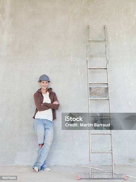 Photo libre de droit de Femme Portant Chapeau Dur Et Sappuyant Sur Un Mur Avec Échelle banque d'images et plus d'images libres de droit de Cadrage en pied