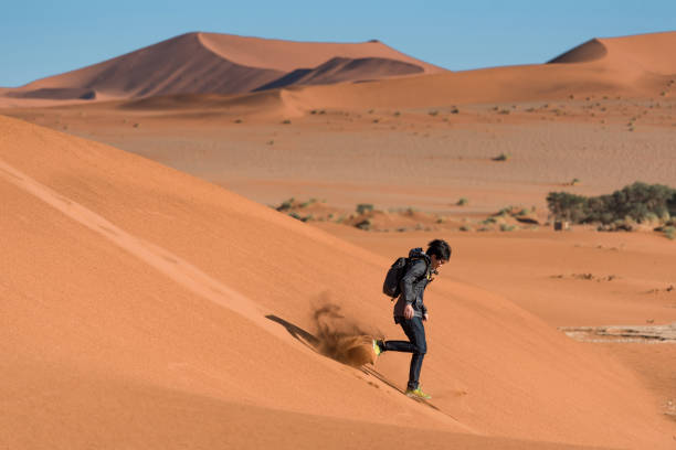 istock Young Asian man carrying backpack running down on sand dune in Namib desert, Namibia 950122336