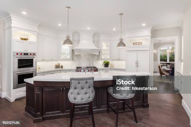 Beautiful Kitchen In New Luxury Home With Island Pendant Lights And Hardwood Floors Has Partial View Of Dining Room Stock Photo - Download Image Now