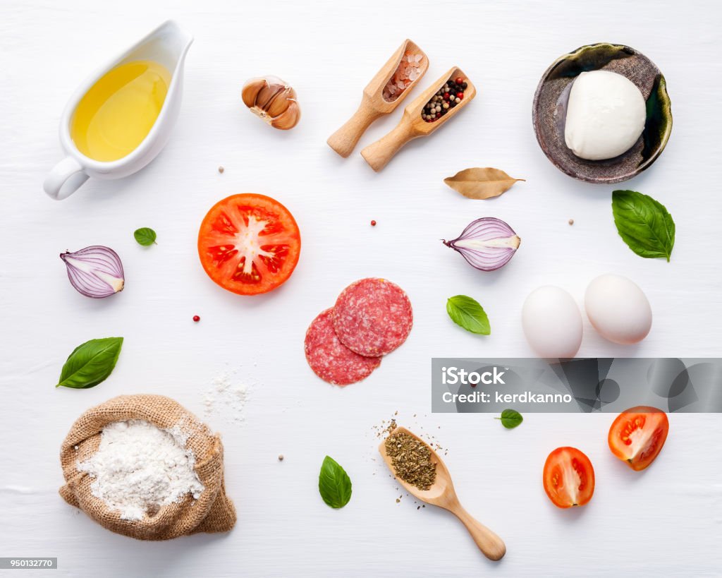 Gli ingredienti per la pizza fatta in casa con ingredienti basilico dolce, pomodoro, aglio, alloro, pepe, cipolla e mozzarella su sfondo bianco in legno con laici piatti. - Foto stock royalty-free di Ingrediente