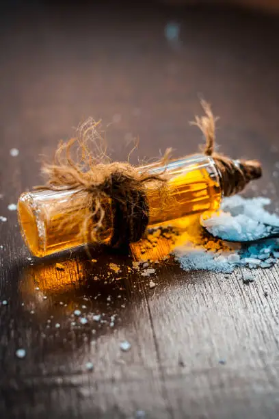 Photo of Close up of aurvedic herb camphor powder in a small spoon and its oil on brown wooden surface in dark Gothic colors is helps in Prevents Skin Infections,Eliminates Gas,Reduces Nervous Disorders etc.