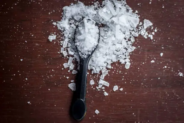 Photo of Close up of aurvedic herb camphor powder in a small spoon on brown wooden surface in dark Gothic colors is helps in Prevents Skin Infections,Eliminates Gas,Reduces Nervous Disorders,Increases Libido.