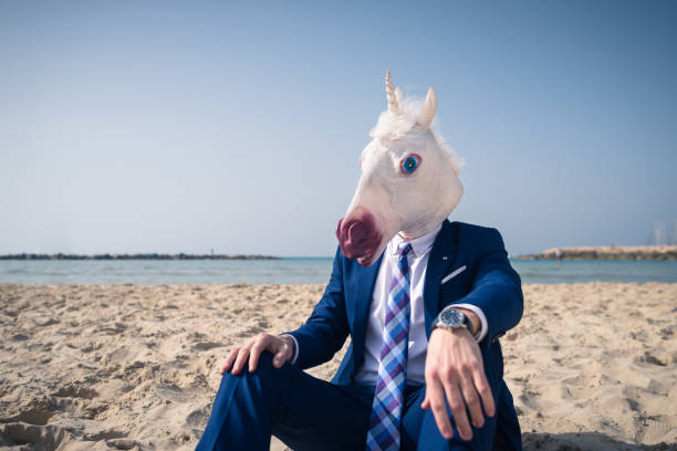 istock Trendy man in funny mask sits on the sand 950178970