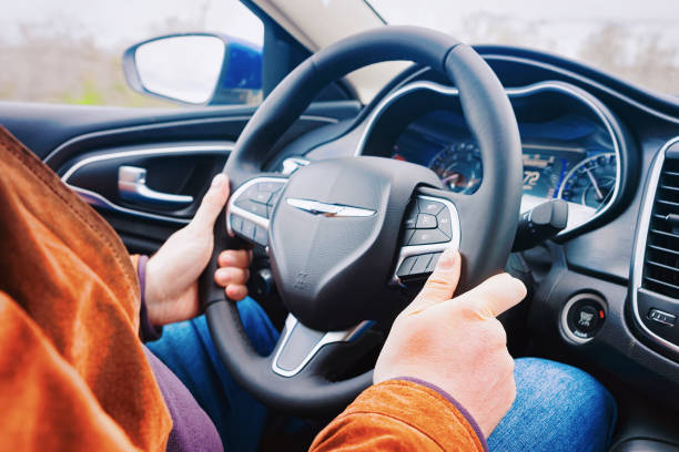A male hand on a car's steering wheel. \n