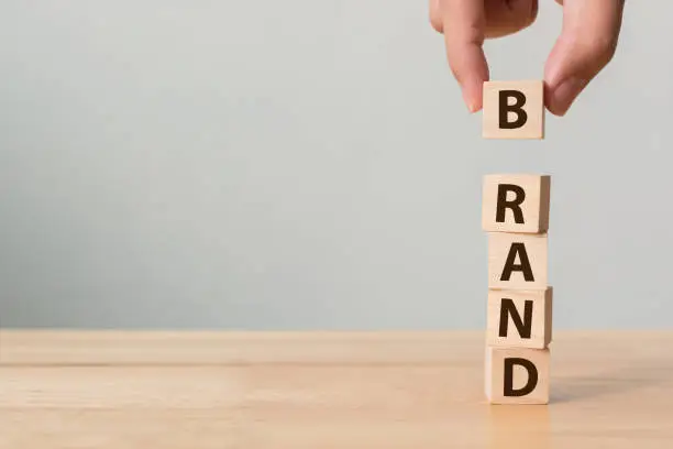 Photo of Hand of male putting wood cube block with word “BRAND” on wooden table. Brand building for success concept