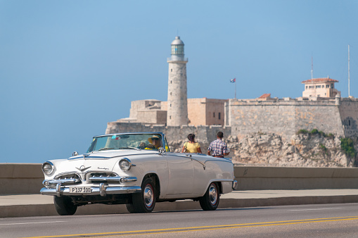 Classic convertible car generally used for sightseeing tours on Avenida del Malecón in Old Havana, with the entrance lighthouse El Morro in the background. Havana Cuba May 14, 2015