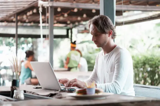 Young male freelancer sitting in outdoor cafe working in laptop