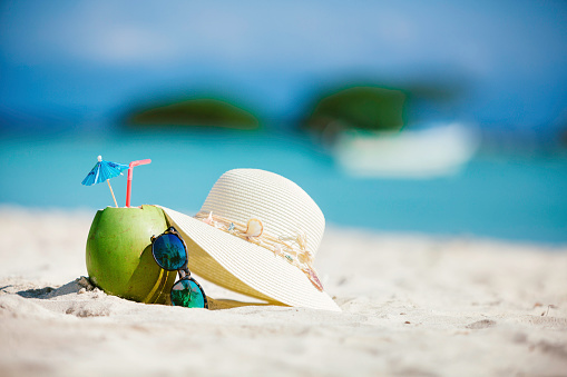 Coconut tropical drink with sunglasses and female hat on sand in a Caribbean island turquoise beach
