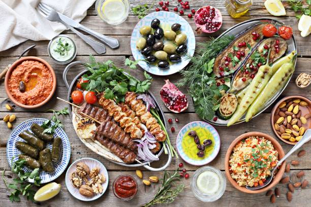 Middle eastern, arabic or mediterranean dinner table with grilled lamb kebab, chicken skewers with roasted vegetables and appetizers variety serving on rustic outdoor table. Middle eastern, arabic or mediterranean dinner table with grilled lamb kebab, chicken skewers with roasted vegetables and appetizers variety serving on rustic outdoor table. Overhead view. mediterranean food photos stock pictures, royalty-free photos & images
