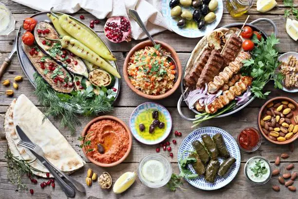 Middle eastern, arabic or mediterranean dinner table with grilled lamb kebab, chicken skewers  with roasted vegetables and appetizers variety serving on rustic outdoor table. Overhead view.