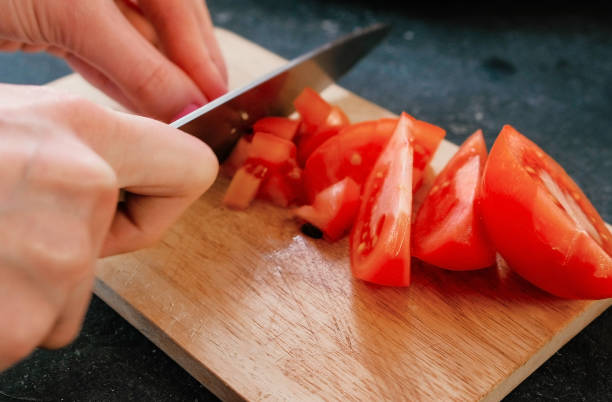 istock Closeup woman's hands cutting tomatoes on a wood board. 950253502