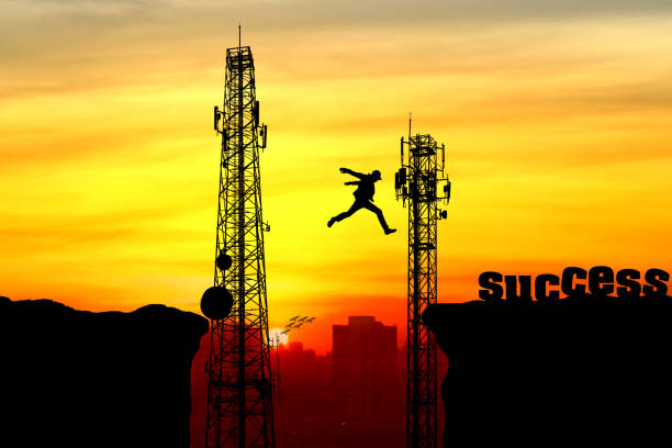 istock Silhouette of a man jumping over the cliff and Telecommunication tower 950256556