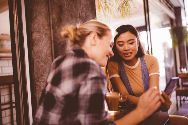 スマート フォンを見て、コーヒーを飲みながらカフェで若い女性 - 会話 楽しい ストックフォトと画像