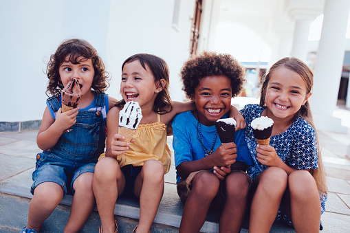 Grupo de alegres niños multiétnicos comiendo helado en verano photo