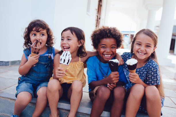 Group of cheerful multi-ethnic children eating ice-cream in summer Multi-ethnic best friends children eating ice-cream and having fun on summer holidays licking photos stock pictures, royalty-free photos & images