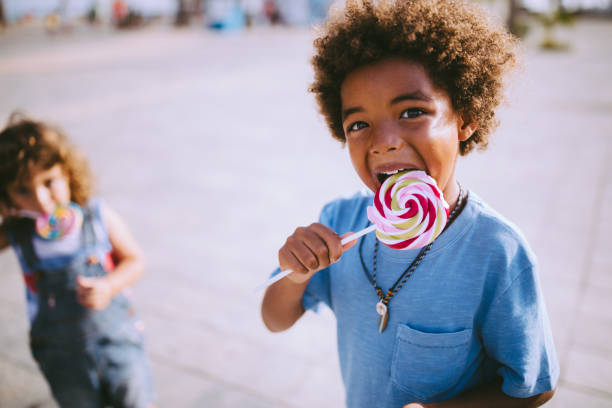 Multi-ethnic brothers eating colourful lollipops outdoors in summer Multi-ethnic children friends with curly hair and colourful lollipops outdoors on summer vacations candy in mouth stock pictures, royalty-free photos & images