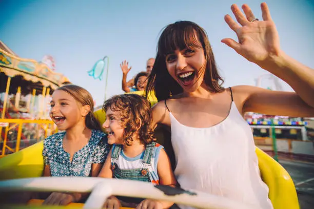 Happy multi-ethnic children having fun with parents on roller coaster amusement park ride in summer