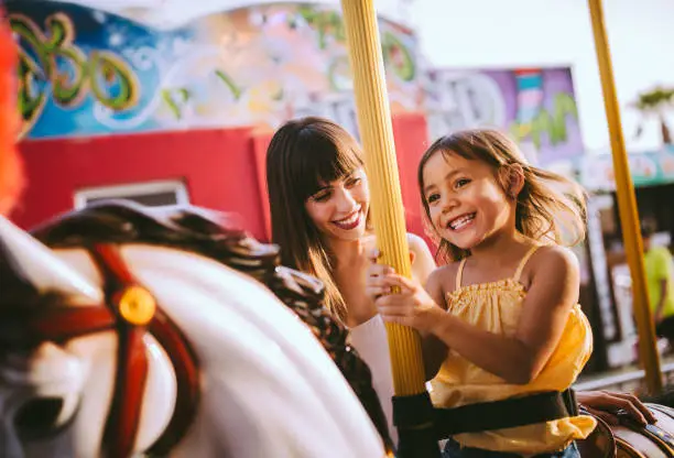Mixed-race family with daughter and mother having fun on merry-go-round amusement park ride in summer